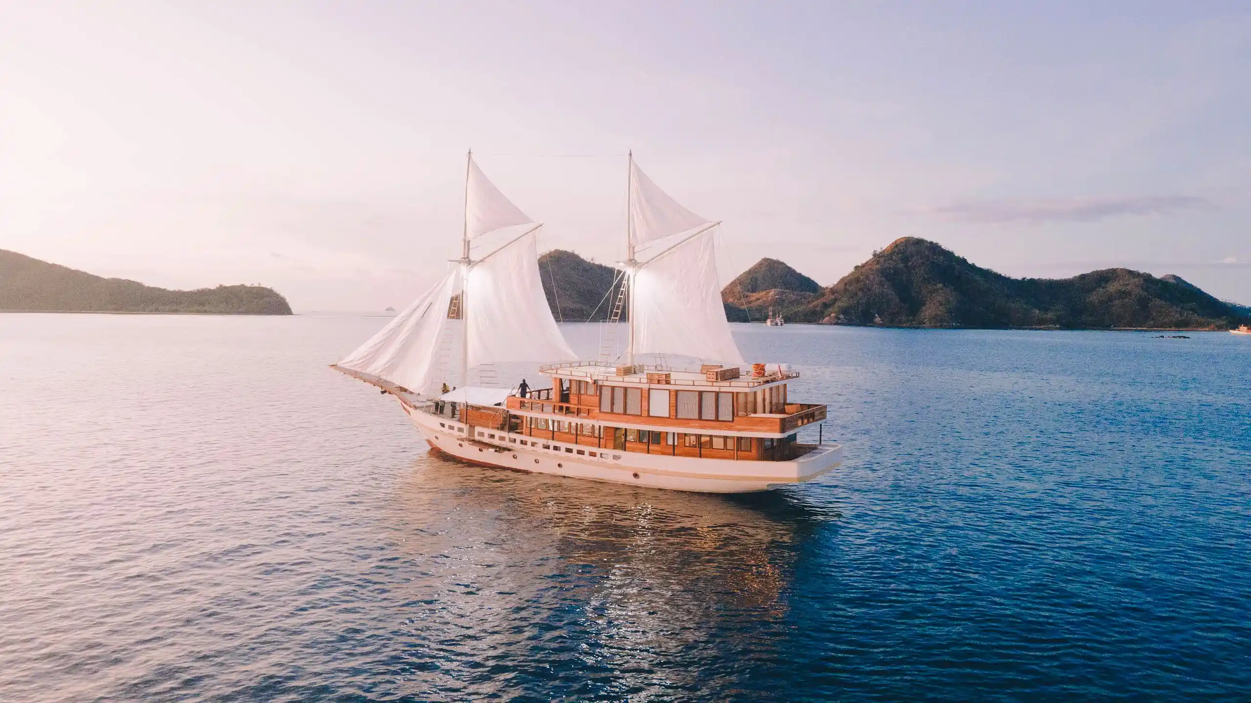 The wooden phinisi Elbark under full sail at golden hour off the Komodo islands